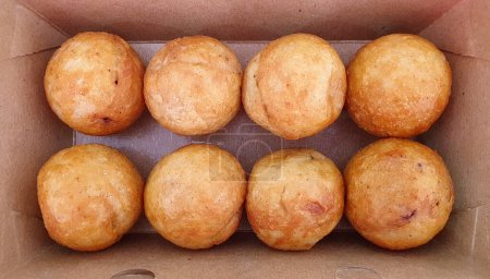 Takoyaki is a ball-shaped Japanese octopus dumpling snack made of a wheat flour-based batter and cooked in a special molded pan. Close up of plain takoyaki balls in paper plate before putting toppings