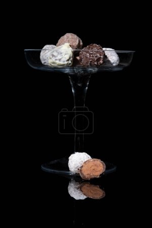 Photo for Fine truffle chocolates on a high glass bowl. On reflective black background and black background - Royalty Free Image