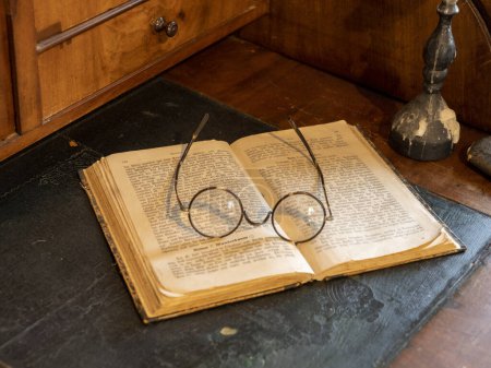 Photo for Still life of open book with old German writing, round reading glasses and candlestick on antique secretary - Royalty Free Image