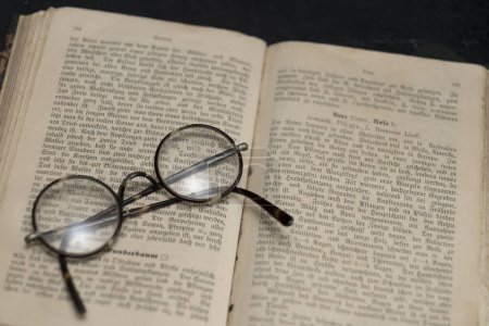 Nahaufnahme eines antiquarischen Buches mit altdeutscher Schrift und Lesebrille mit aufliegenden runden Gläsern