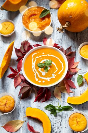 Pumpkin soup and muffins with the dry autumn leaves on white wooden background