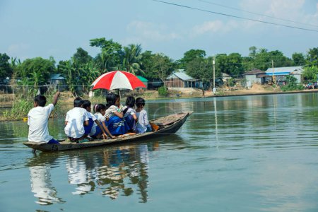 Photo for Taherpur, Bangladesh - November 05, 2019: School children wearing school uniforms are going to attend school by crossing a big river rowing a boat due to flood. - Royalty Free Image