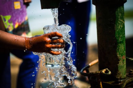 Selektiver Fokus auf die Mädchenhände, die ein Glas halten, um frisches Trinkwasser zu sammeln. Kinder trinken reines Wasser aus lokalem Rohrbrunnen