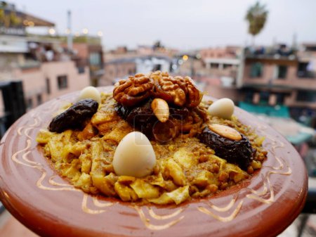 Téléchargez les photos : Rfissa, un plat marocain de poulet cuit, lentilles et oignons servis sur un lit de sperme râpé, Marrakech Médina en arrière-plan. Photo de haute qualité - en image libre de droit