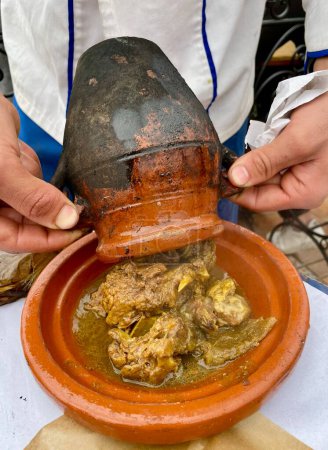 Téléchargez les photos : Homme versant Tangia, Tanjia, un plat local de Marrakech, agneau rôti cuit dans des pots d'argile, dans une assiette en céramique. Marrakech, Maroc. Photo de haute qualité - en image libre de droit