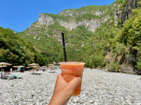 Téléchargez les photos : Main tenant délicieux smoothie aux fruits, rivière paradisiaque Shala dans le backgrround, Albanie. Photo de haute qualité - en image libre de droit