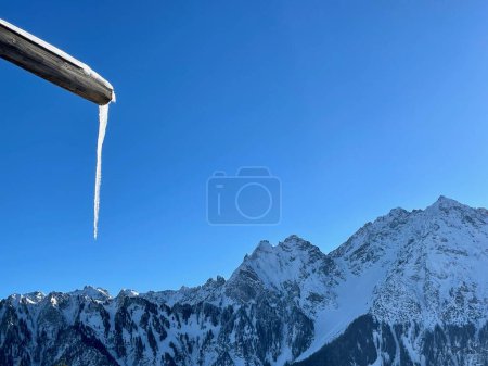 Foto de Icicle colgando de canalón, cielo azul y panorama de montaña en el fondo. Foto de alta calidad - Imagen libre de derechos