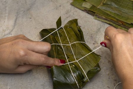 Frauenhände binden einen Hallaka oder Tamale in ein Bananenblatt. Traditionelle Lebensmittel