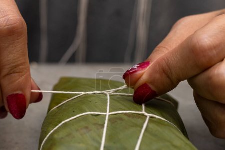 Frauenhände binden einen Hallaka oder Tamale in ein Bananenblatt. Traditionelle Lebensmittel