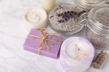 Lavender flowers, fragrant sea salt, body cream and candle. The concept of spa, beauty and health salon, skin care cosmetics. Natural cosmetics.Aroma procedures. Closeup on white marble background.