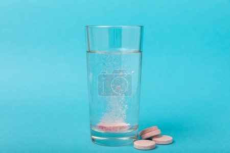Pastillas efervescentes en un vaso de agua sobre un fondo azul. Vitaminas. Concepto de salud. Drogas de inmunidad. Espacio para copia. Espacio para texto.