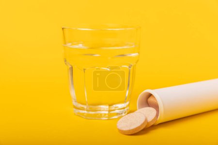 Téléchargez les photos : Un comprimé vitaminé effervescent tombe et se dissout dans un verre d'eau sur fond jaune. Le concept de santé. Concept de médecine. Place pour le texte. - en image libre de droit