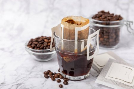 Foto de Making drip coffee with a special taste against the background of coffee beans. Drip coffee bag in a coffee cup. Trends in brewing coffee at home.Drip coffee filter. Flatley. Copy space. Place for text. - Imagen libre de derechos