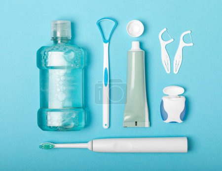 Photo for Electronic ultrasonic toothbrush, mouthwash, floss, tongue cleaner and toothpaste on blue textured background. Items for dental care and caries prevention in the bathroom. Dentistry concept. Copy space. - Royalty Free Image