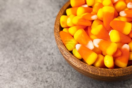 Candy corn. Classic white, orange and yellow Halloween lollipops. Sweet pumpkin gummies in a wooden bowl on a black marble background.Copy space.Place for text. Holiday concept.