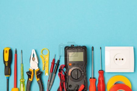 Electrician equipment on blue background with copy space.Top view.Electrician tool set.Multimeter, tester,screwdrivers,cutters,duct tape,lamps,tape measure and wires.Flet lay.