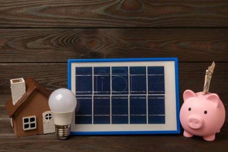 Composición plana con panel solar, lámpara led y alcancía sobre fondo marrón. El concepto de ahorro de dinero y energía limpia. El concepto de ecología y desarrollo sostenible.