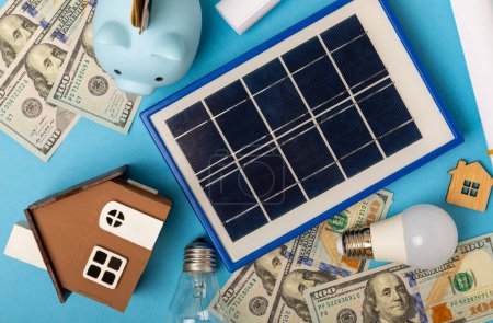 Composición plana con panel solar, lámpara led y alcancía sobre fondo azul. El concepto de ahorro de dinero y energía limpia. El concepto de ecología y desarrollo sostenible.