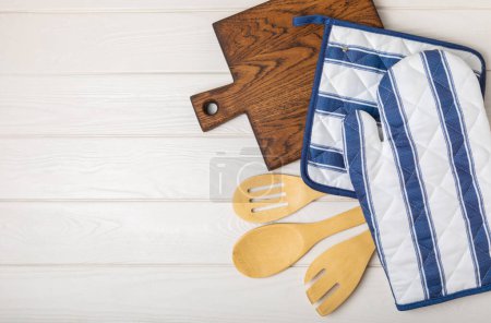 Utensilios de cocina de madera, tabla de cortar, agarradera y guante en la mesa, vista superior. Manopla de cocina y guantes protectores del horno en la mesa. Utensilios de cocina. Accesorios.Close-up.top view de la cocina.