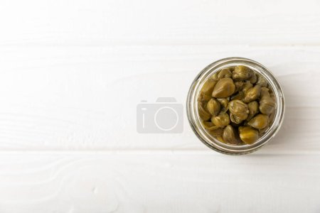 Capers in a bowl on a wooden kitchen table. Capers with sea salt and rosemary. Pickled capers.Mediterranean cuisine ingredient. Organic spices and seasonings. Copy space.