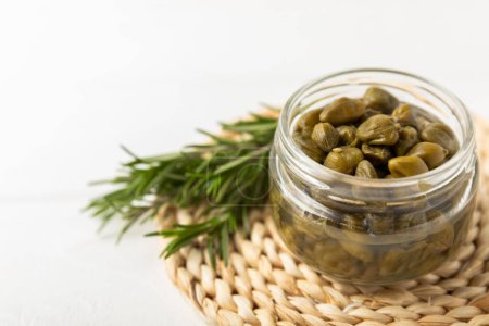 Capers in a bowl on a wooden kitchen table. Capers with sea salt and rosemary. Pickled capers.Mediterranean cuisine ingredient. Organic spices and seasonings. Copy space.