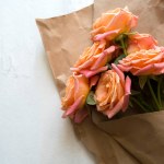 Gift, flowers, craft packaging. Orange-pink roses in kraft paper on a white wooden background