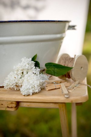 Téléchargez les photos : Lavage, entretien des tissus, détergents. Lavage dans le jardin en été - lavabo en métal blanc avec de l'eau sur une table brune en bois, pinces à linge en bois, linge, corde - en image libre de droit
