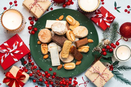 Photo for Top view of Nougat christmas sweet,mantecados and polvorones with christmas ornaments on a plate over christmas tablecloth. Assortment of christmas sweets typical in Spain - Royalty Free Image