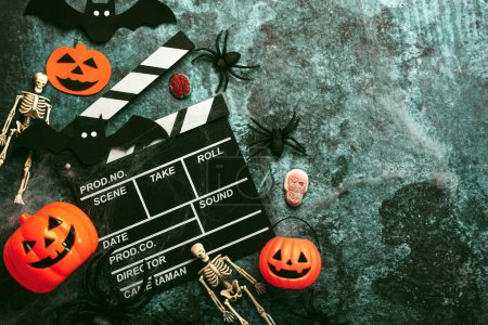 Halloween movies concept. Movie clapperboard with funny halloween pumpkin,skeletons and spiders over grunge background. Halloween concept background