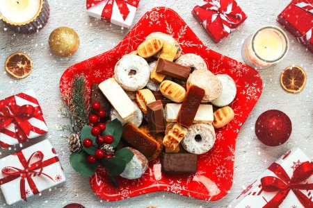 Photo for Top view of Nougat christmas sweet,mantecados and polvorones with christmas ornaments on a christmas star shaped red plate over white background. Assortment of christmas sweets typical in Spain - Royalty Free Image