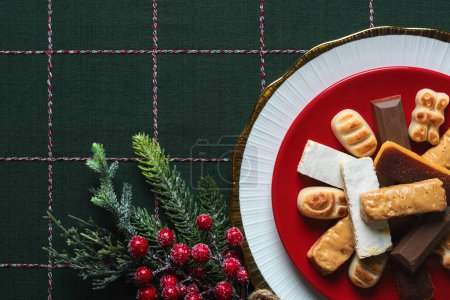 Photo for Top view of Nougat christmas sweet with christmas ornaments on a plate on a christmas tablecloth. Assortment of christmas sweets typical in Spain - Royalty Free Image