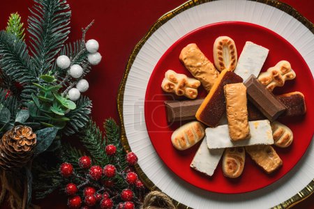 Photo for Top view of Nougat christmas sweet with christmas ornaments on a plate over a red background. Assortment of christmas sweets typical in Spain - Royalty Free Image