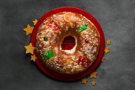 Vista superior de Roscon de reyes sobre un plato rojo con estrellas doradas. Concepto del día de Reyes pastel español de tres reyes sobre fondo gris. Concepto Reyes día español pastel de tres reyes