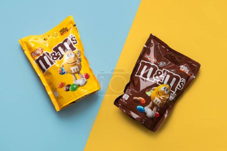 Téléchargez les photos : Gros plan de paquets de M & M de chocolat et d'arachide sur fond bleu et jaune. Éditorial illustratif - en image libre de droit