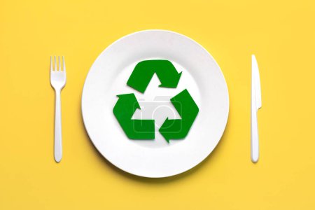Draufsicht auf das Symbol des Recyclings mit weißem Plastikbesteck und Teller über gelbem Hintergrund. Umweltfreundliches Recyclingkonzept