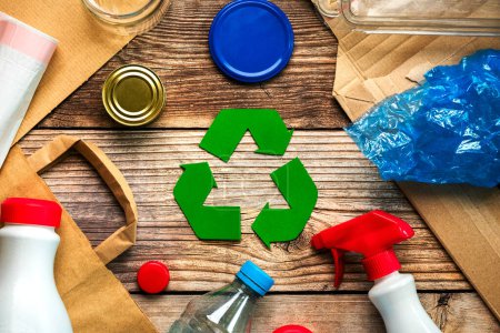 Draufsicht auf das Symbol des Recyclings mit verschiedenen Müllmaterialien auf einem Holztisch. Umweltfreundliches Recyclingkonzept