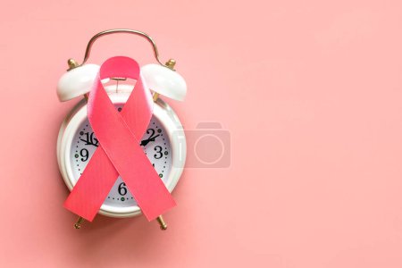 Draufsicht auf das rosafarbene Band-Symbol des Brustkrebses auf einem weißen Wecker mit Platz für Text auf rosa Hintergrund. Brustkrebs-Aufklärungskonzept