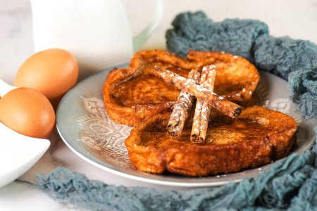 Plate with traditional homemade Torrijas, cinnamon stick,milk and eggs on a marble table. Typical Lent and Easter dessert in Spain