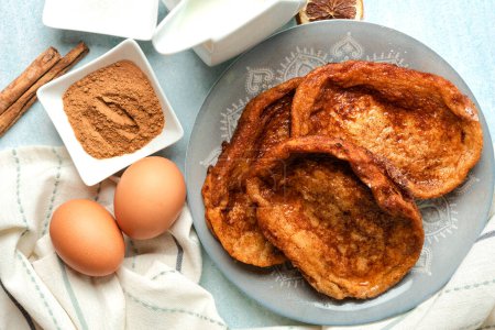Plate with traditional homemade Torrijas, cinnamon,milk and eggs on a blue table. Typical Lent and Easter dessert in Spain