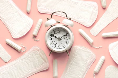 Top view of sanitary pads, menstrual tampons and white alarm clock over pink background. Concept of menstruation and menopause