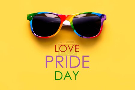 Closeup of LGTBI flag sunglasses with the text Love, Pride day over yellow background. LGBT Pride concept