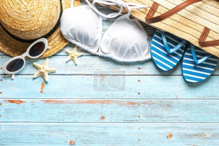 Top view of beach bag, straw hat, sunglasses, flip flops and bikini with copy space for text on a background of wooden boards. Summer holiday concept