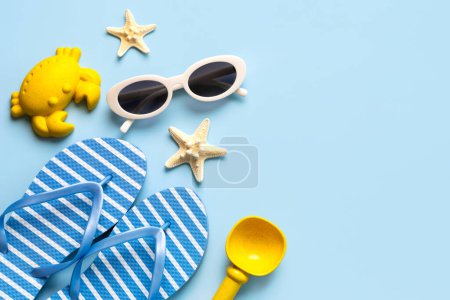Top view of flip flops,sunglasses, starfish and beach toys with copy space for text over blue background. Summer holiday concept
