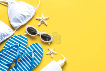 Top view of flip flops,sunglasses,starfish,bikini,and sunscreen with copy space for text over yellow background. Summer holiday concept