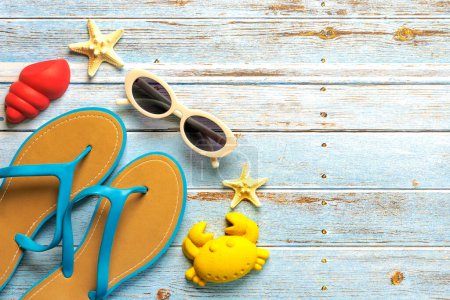 Top view of flip flops,sunglasses, starfish and beach toys with copy space for text on a background of wooden boards. Summer holiday concept
