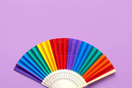 Closeup of LGTBI flag folding wooden open hand fan with copy space for text over purple background. LGBT Pride concept