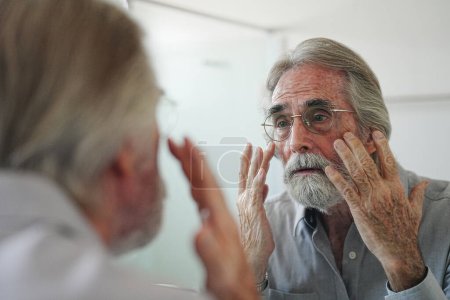 Photo for Old man with gray hair checking hair in front of mirror - Royalty Free Image