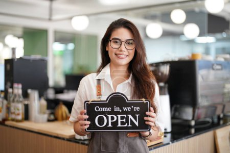 Photo for Portrait of happy woman standing in her store. Cheerful waitress waiting for clients at coffee shop. Successful small business owner in casual wearing grey apron - Royalty Free Image