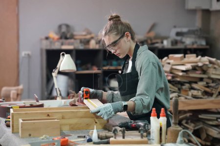 Junge schöne Frau bei der Arbeit in der Schreinerei DIY Werkstatt. Kleinunternehmerin, junge Frau, die in einer Möbelfabrik arbeitet.