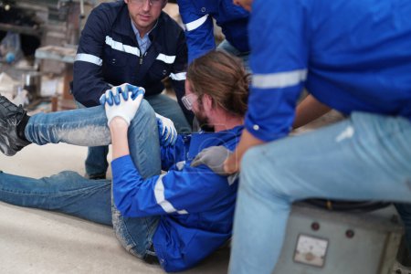 Téléchargez les photos : Travailleur victime d'un accident du travail à l'usine et collègue qui l'aide alors qu'il est blessé à la jambe. - en image libre de droit